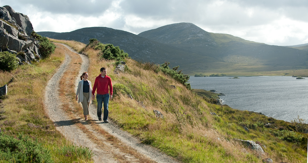 Couple walks a scenic lakeside trail surrounded by hills at Glenveagh National Park, County Donegal.